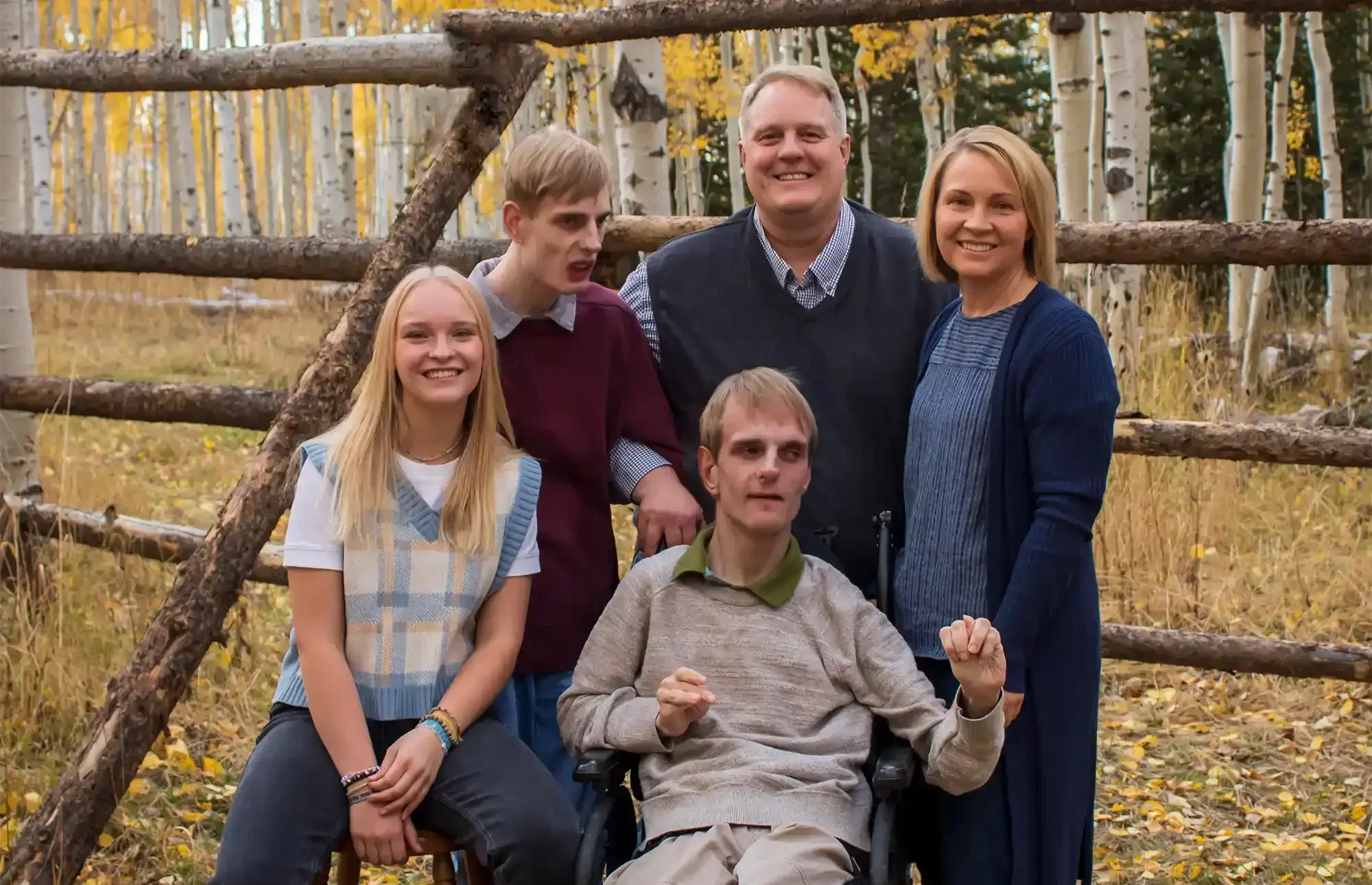 A family of five posing outdoors with a wooden fence and greenery.