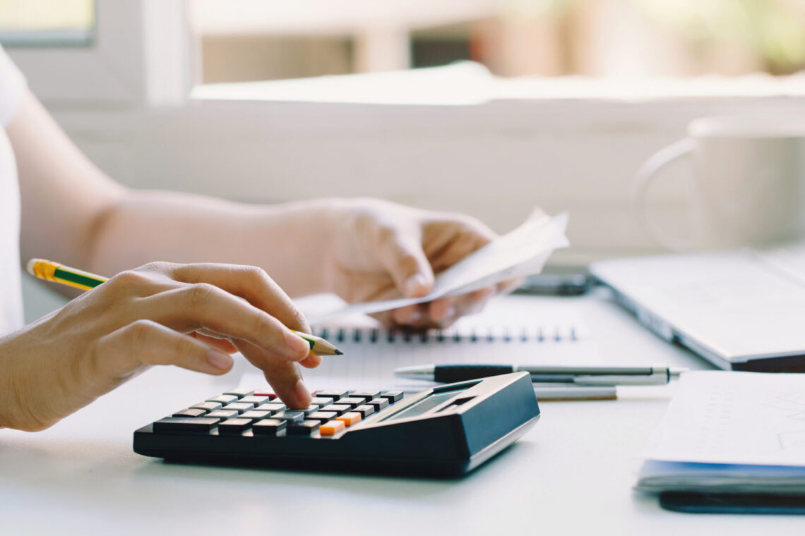 Person using a calculator and holding a pen for financial work.